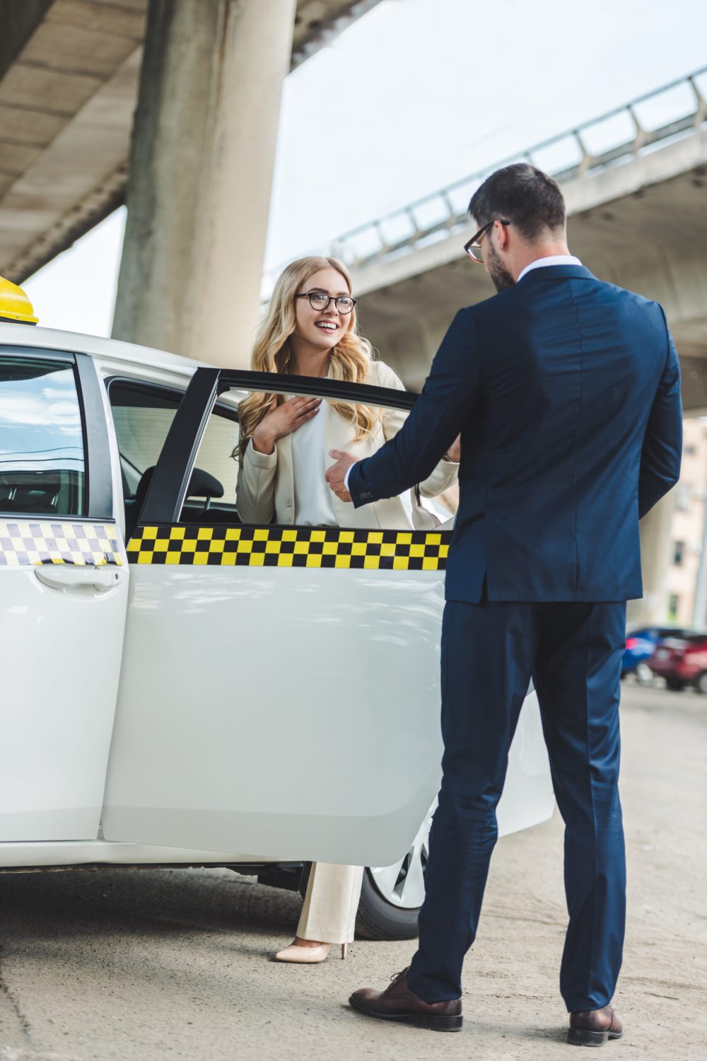 man in suit opening car door to beautiful smiling woman sitting in taxi